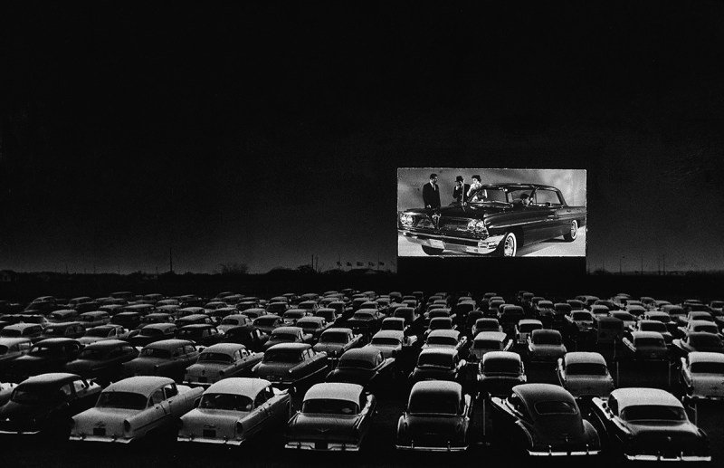 Vehicles fill a drive-in theater while people on the screen stand near a new car, 1950s. (Photo by New York Times Co./Hulton Archive/Getty Images)