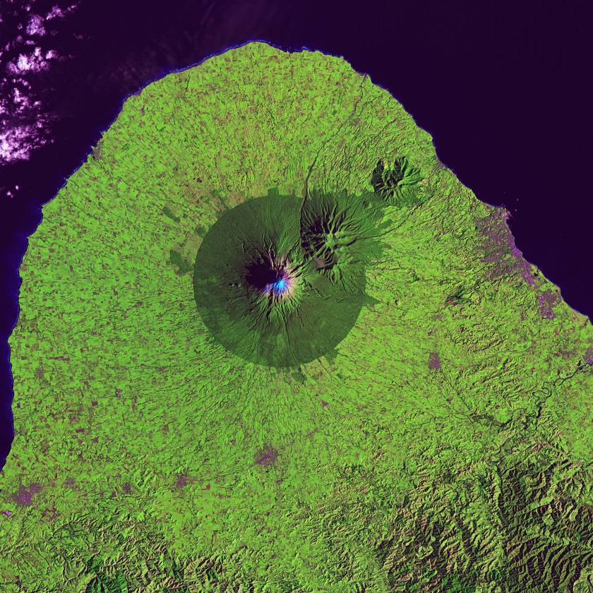 A nearly perfect circle of forest delineates the boundary of Egmont National Park in New Zealand. Snow-capped Mount Taranaki marks the center of the park, which is surrounded by green farmland. (USGS/NASA)