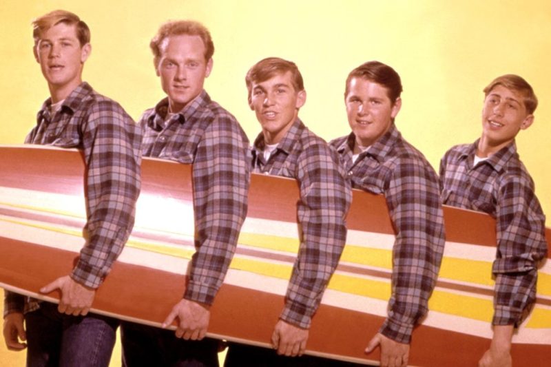 LOS ANGELES - AUGUST 1962: Rock and roll band "The Beach Boys" pose for a portrait with a surfboard in August 1962 in Los Angeles, California. (L-R) Brian Wilson, Mike Love, Dennis Wilson, Carl Wilson, David Marks. (Photo by Michael Ochs Archives/Getty Images)