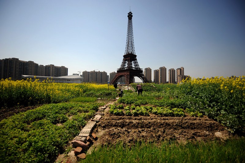 HANGZHOU, CHINA - MARCH 21: (CHINA OUT) Farmers work in front of a replica of The Eiffel Tower standing at 108 metres at Tianducheng residential community, also known as a knockoff of Paris, on March 21, 2014 in Hangzhou, China. Tianducheng is developed by Zhejiang Guangsha Co. Ltd.. The construction began in 2007 with a replica of the Eiffel Tower and Parisian houses, and it is expected to be completed by 2015. (Photo by VCG/VCG via Getty Images)