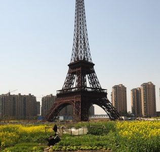 HANGZHOU, CHINA - MARCH 21:  (CHINA OUT) Farmers work in front of a replica of The Eiffel Tower standing at 108 metres at Tianducheng residential community, also known as a knockoff of Paris, on March 21, 2014 in Hangzhou, China. Tianducheng is developed by Zhejiang Guangsha Co. Ltd.. The construction began in 2007 with a replica of the Eiffel Tower and Parisian houses, and it is expected to be completed by 2015.  (Photo by VCG/VCG via Getty Images)