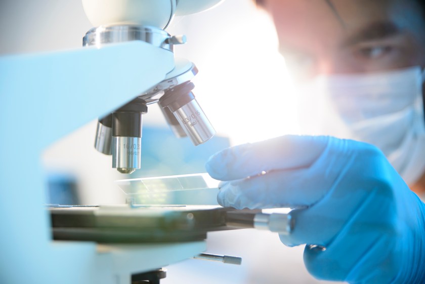 A scientist placing a slide under a microscope (Getty Images)