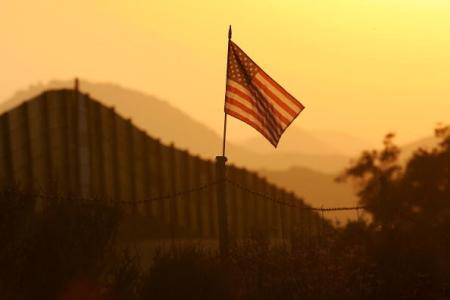 CAMPO, CA - OCTOBER 08:  A U.S. flag put up by activists who oppose illegal immigration flies near the US-Mexico border fence in an area where they search for border crossers October 8, 2006 near Campo, California. The activists want the fence expanded into a fully-lit double-fenced barrier between the US (R) and Mexico. US Fish and Wildlife Service wardens and environmentalists warn that a proposed plan by US lawmakers to construct 700 miles of double fencing along the 2,000-mile US-Mexico border, in an attempt to wall-out illegal immigrants, would also harm rare wildlife. Wildlife experts say cactus-pollinating insects would fly around fence lights, birds that migrate by starlight in the desert wilderness would be confused, and large mammals such as jaguars, Mexican wolves, Sonoran pronghorn antelope, and desert bighorn sheep would be blocked from migrating across the international border, from California to Texas.  (Photo by David McNew/Getty Images)