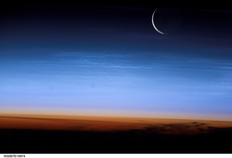 Silvery-blue noctilucent clouds extend far above the Earth's troposphere. The sliver of the setting moon is visible at upper right (NASA/Getty Images)