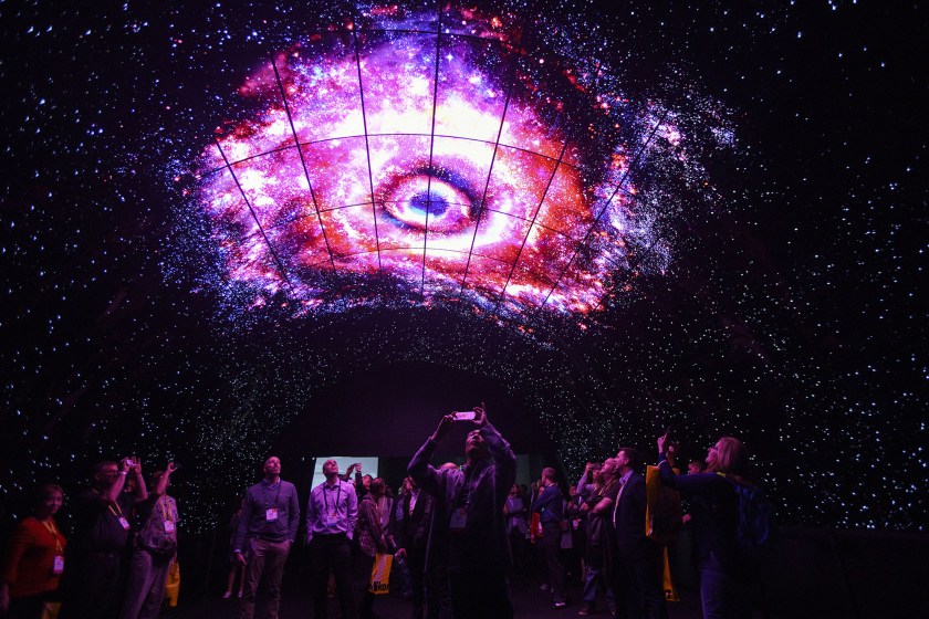 Attendees take photographs with mobile devices while standing under a tunnel wall of LG OLED 4K TVs during the 2017 Consumer Electronics Show (CES) in Las Vegas, Nevada, U.S., on Thursday, Jan. 5, 2017. CES, celebrating its 50th year, will showcase self-driving cars, TVs, drones, robots and a slew of other gadgets. Photographer: Patrick T. Fallon/Bloomberg via Getty Images