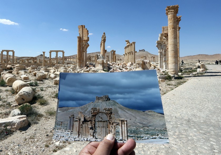 A general view taken on March 31, 2016 shows a photographer holding his picture of the Arc du Triomphe (Triumph's Arch) taken on March 14, 2014 in front of the remains of the historic monument after it was destroyed by Islamic State (IS) group jihadists in October 2015 in the ancient Syrian city of Palmyra. (Joseph Eid/AFP/Getty Images)