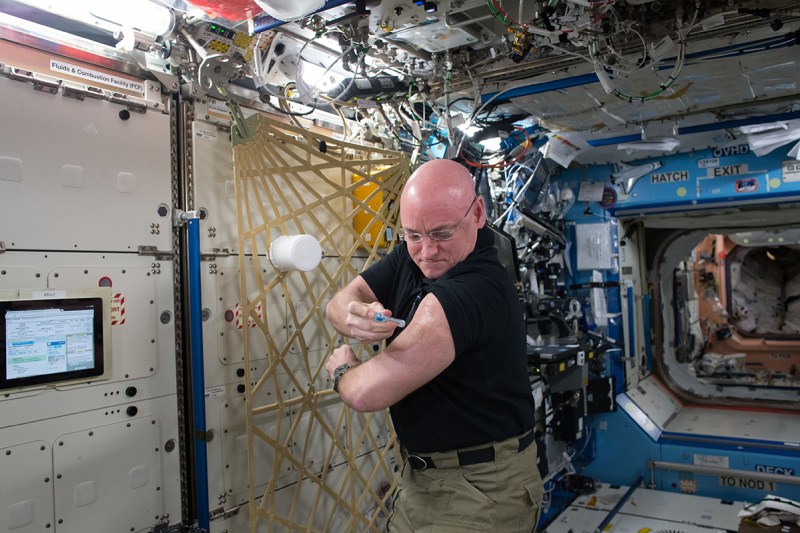 In this Sept. 24, 2015 photo made available by NASA, astronaut Scott Kelly gives himself a flu shot aboard the International Space Station for an ongoing study on the human immune system. The vaccination is part of NASA's Twins Study, a compilation of multiple investigations that take advantage of a unique opportunity to study identical twin astronauts Scott and Mark Kelly, while Scott spends a year aboard the station and Mark remains on Earth. (NASA via AP)