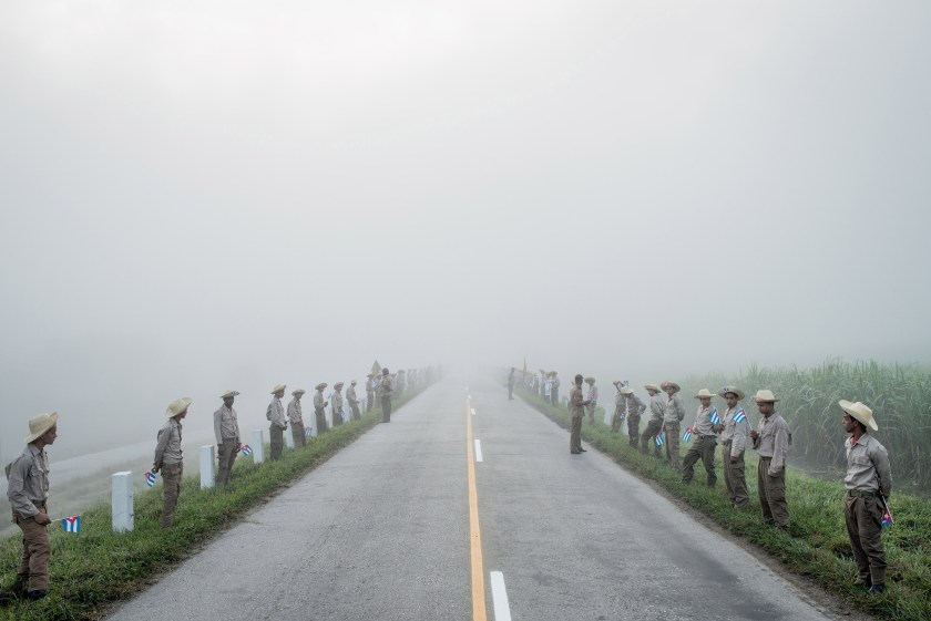 Daily Life - First Prize, Stories: Members of the Ejercito Juvenil del Trabajo waited along the road to Santiago de Cuba at dawn for Fidel Castro’s caravan on December 3, 2016. Cuba declared nine days of mourning after Fidel Castro’s death, a period that culminated with his funeral. In December, days after Fidel Castro’s death, his ashes were taken into the countryside, on a route that retraced, in reverse, the steps of the revolution he led in 1959. Towns and villages along the route were emptied of residents as thousands tried to catch a glimpse of Castro’s remains. For many, the death of Fidel Castro felt like that of a father. In death, as in life, Fidel Castro demanded reverence. Cuba brims with life, a contrast drawn sharper amid its faded grandeur. From one end of the country to the other, thousands of Cubans waited to bid farewell to Fidel. (Tomas Munita for The New York Times)