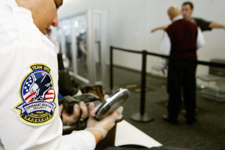 A Transportation Security Administration baggage screener inspects an electronics device as a man is screened in the background at the international terminal of San Francisco International Airport August 5, 2003 in San Francisco, California. The TSA told screeners today to pay close attention to cameras, laptop computers and cell phones, addressing a concern that terrorists could attempt to hide explosives in electronic devices.  (Justin Sullivan/Getty Images)