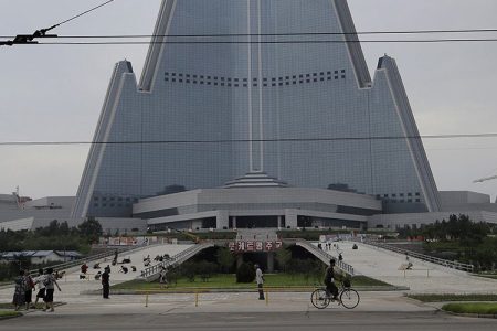 In this Friday, July 28, 2017, photo, people walk past the 105-story pyramid shaped Ryugyong Hotel in Pyongyang, North Korea. Walls set up to keep people out of a construction area around the gargantuan Ryugyong Hotel were pulled down as the North marked the anniversary of the Korean War armistice to reveal two broad new walkways leading to the building and the big red propaganda sign declaring that North Korea is a leading rocket power. (AP Photo/Wong Maye-E)