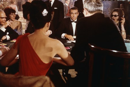 Scottish actor Sean Connery (center) as fictional secret agent James Bond sits at a casino card table in a scene from the film 'Dr. No,' directed by Terence Young, 1962. British actress Eunice Gayson sits with her back to the camera in a red, off the shoulder dress. (MGM Studios/Courtesy of Getty Images)