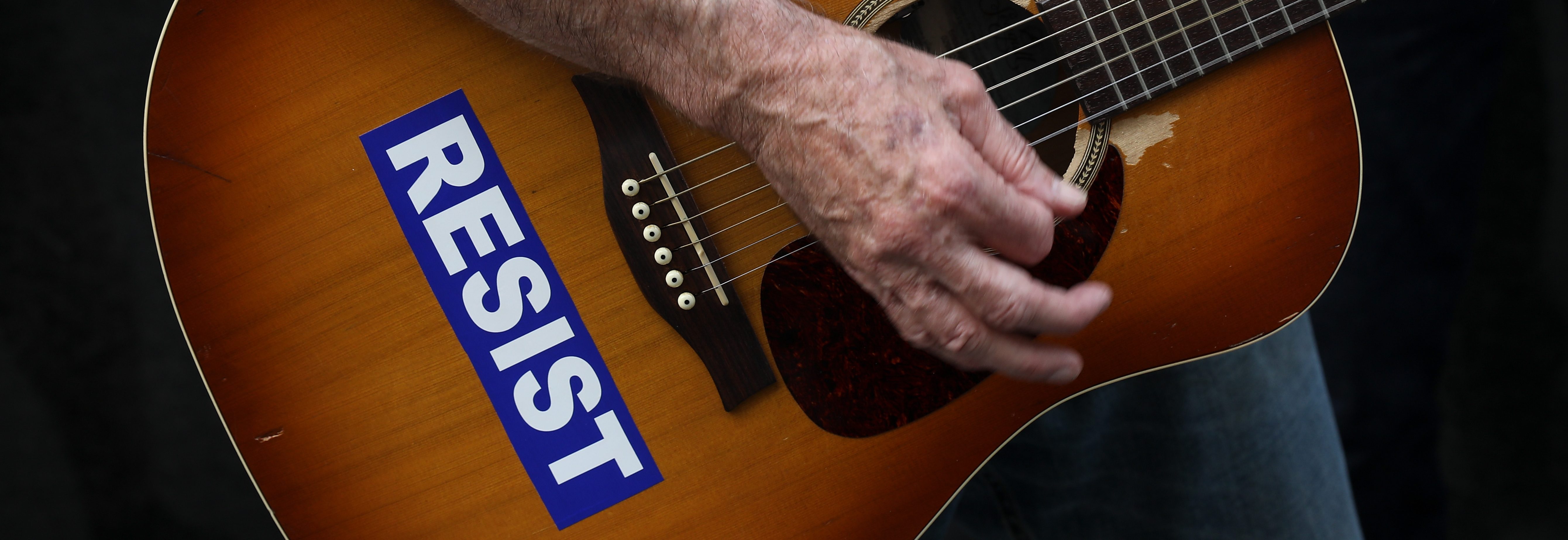 With his guitar adorned with a 'RESIST' sticker, a demonstrator plays music during a gathering to mark the 73rd anniversary of the Hiroshima and Nagasaki nuclear bombings, outside the Japanese Consulate in Midtown Manhattan, August 3, 2018 in New York City. (Photo by Drew Angerer/Getty Images)