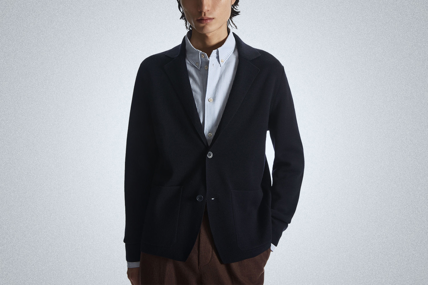 a model in a navy COS knit travel blazer on a grey background