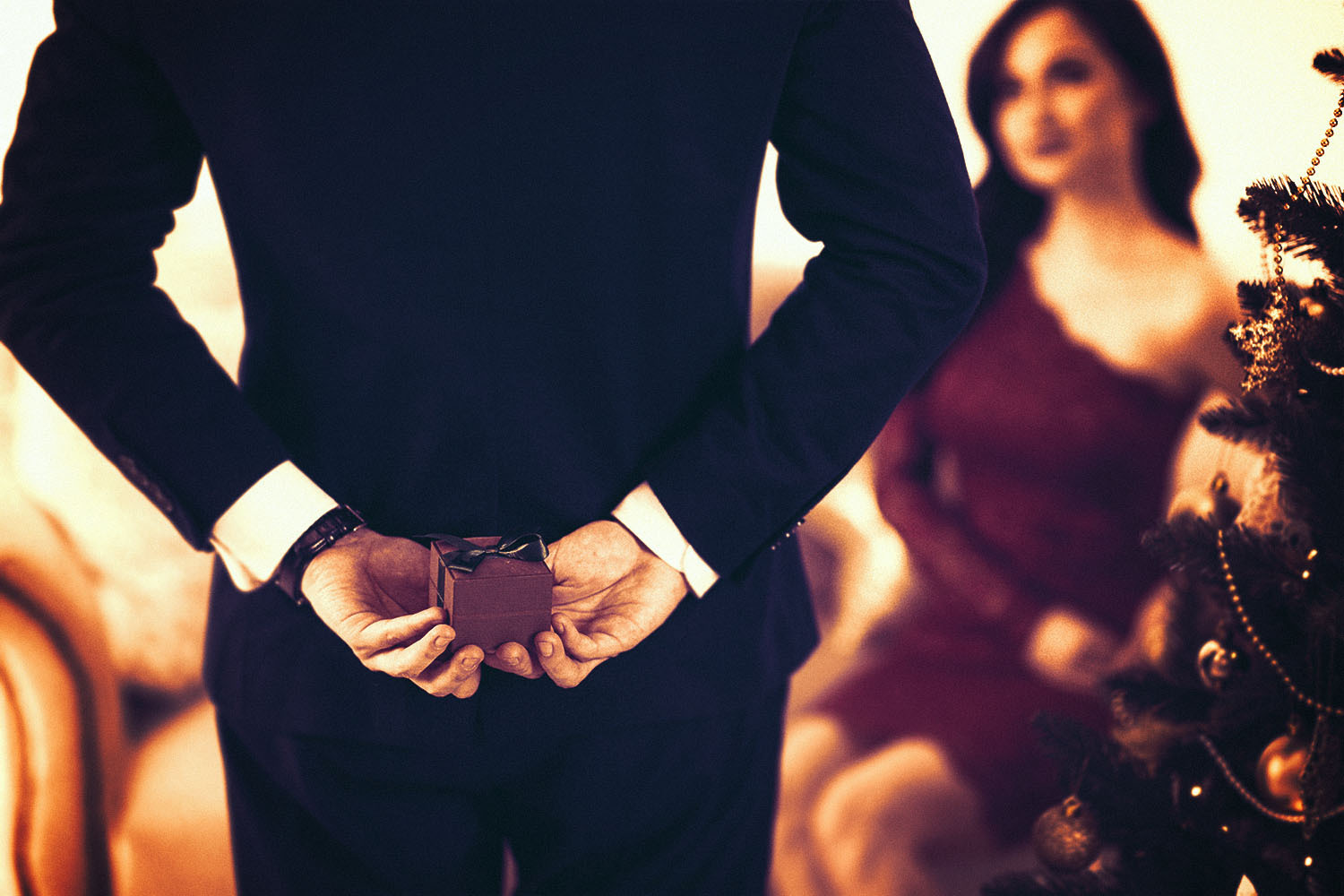 A man holds an engagement ring box behind his back