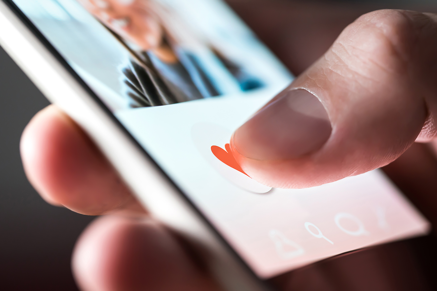 Close up photo shows someone holding a smart phone with a dating app displayed on the screen