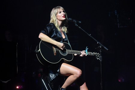 Taylor Swift in black playing a guitar at a concert