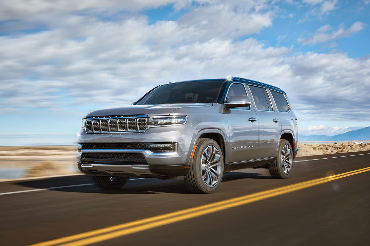 A blue 2022 Jeep Grand Wagoneer SUV shot from the front left driving down the road