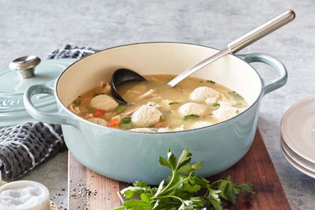 The round wide Dutch oven from Le Creuset filled with soup sitting on a cutting board