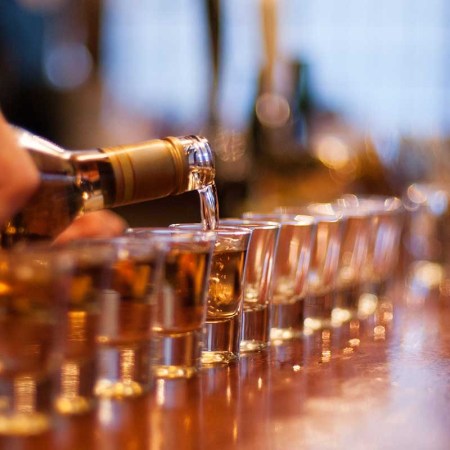 Alcohol being poured into a line of shot glasses set up on a bar