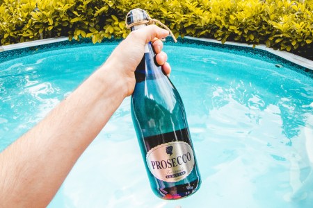 man holding bottle of prosecco with a pool in the background