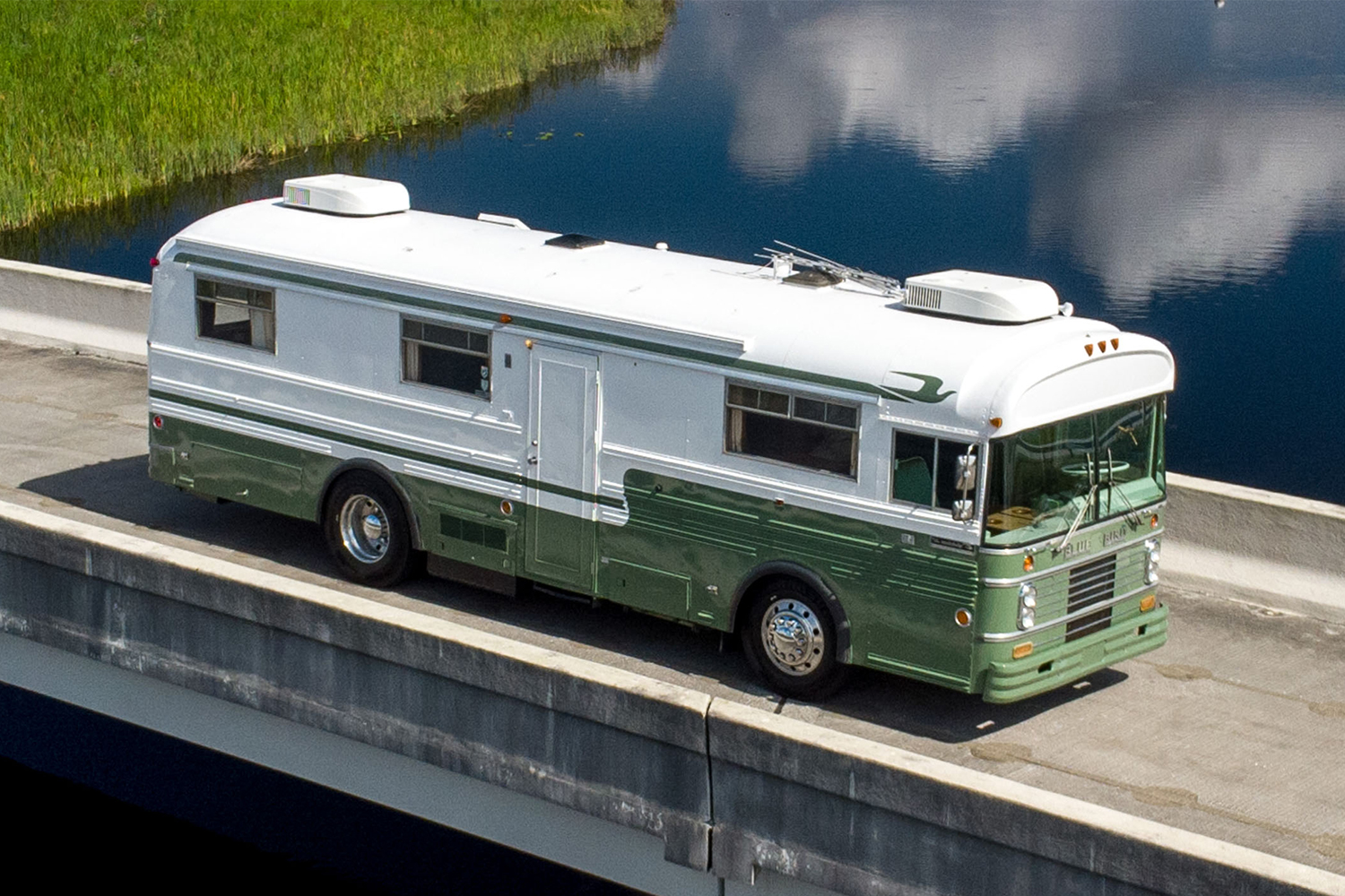 A white and green 1969 Blue Bird Wanderlodge RV sitting on a bridge