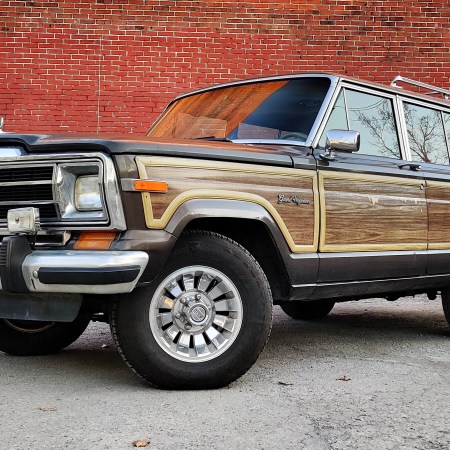 A 1987 Jeep Grand Wagoneer sitting in front of a red brick wall