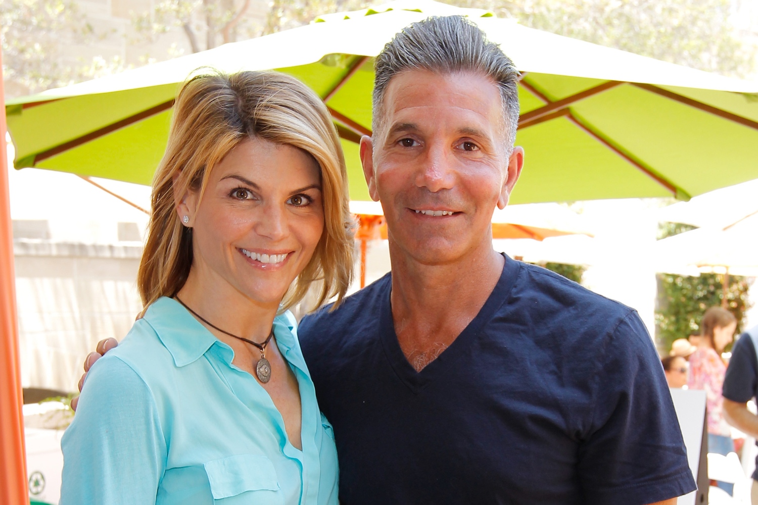 Lori Loughlin and Mossimo Giannulli pose outdoors under green sun umbrella