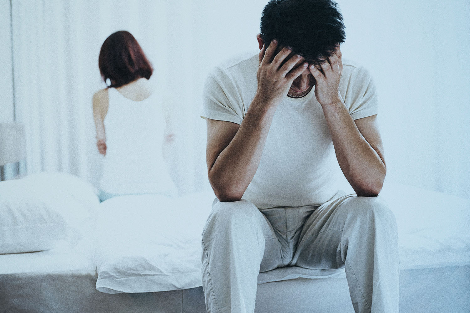 Man and woman sit facing away from each other on either side of the bed looking displeased