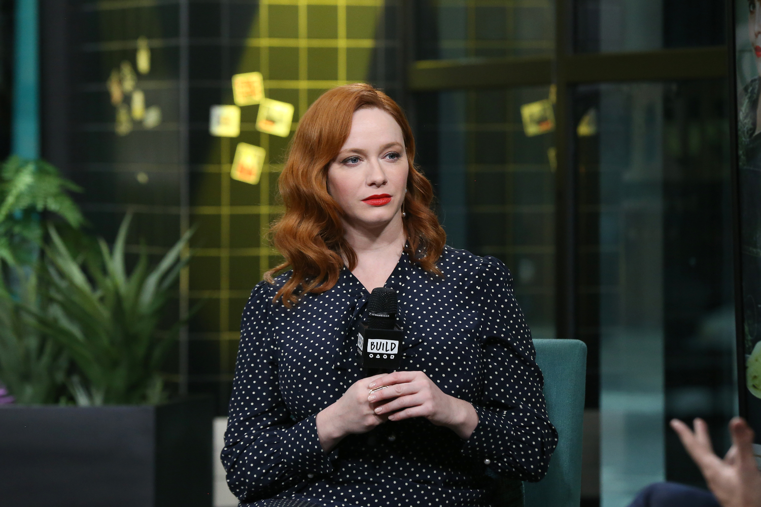 Christina Hendricks holds a microphone on stage, unsmiling