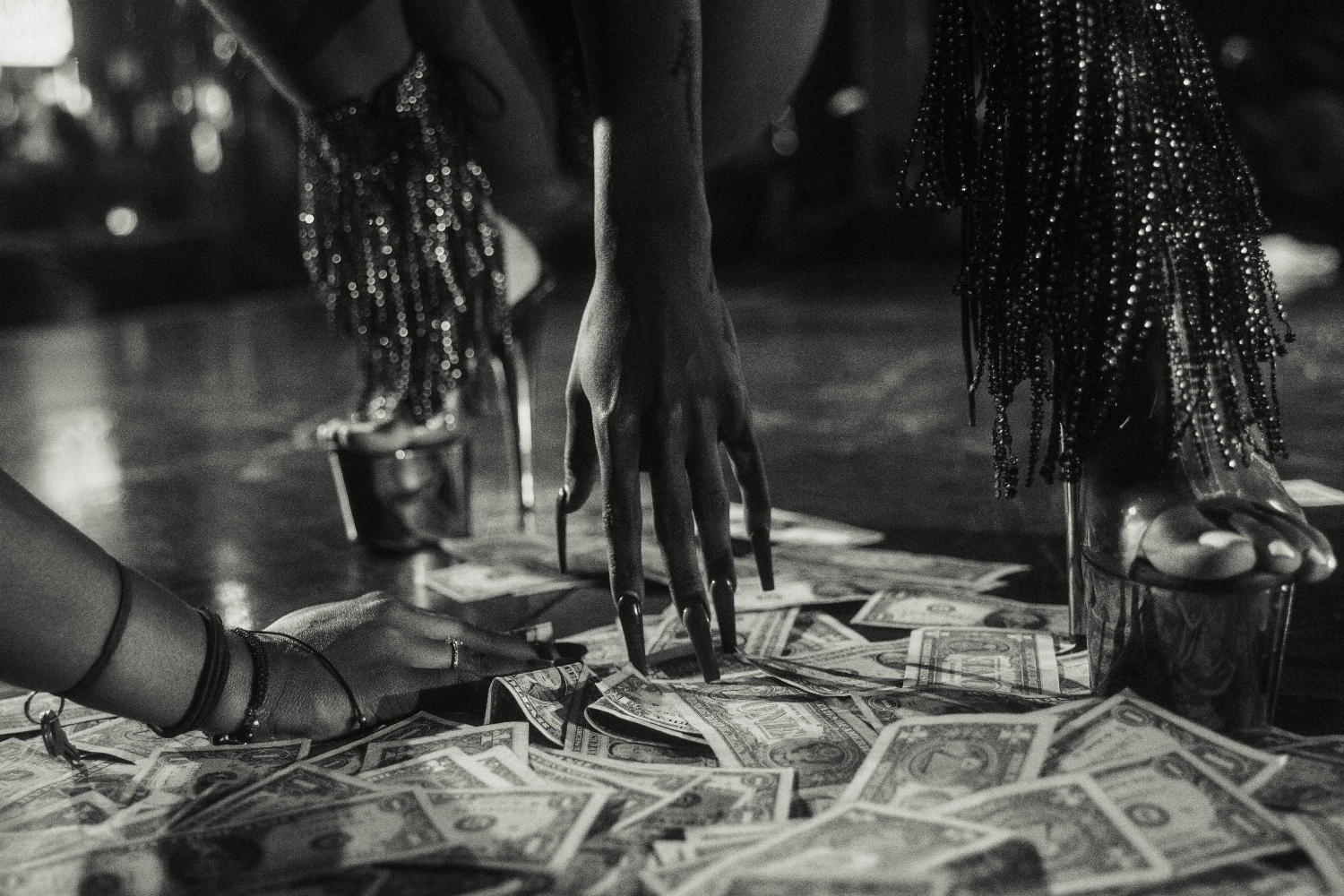 Black and white photo shows a stripper's hand touching the floor, covered in dollar bills