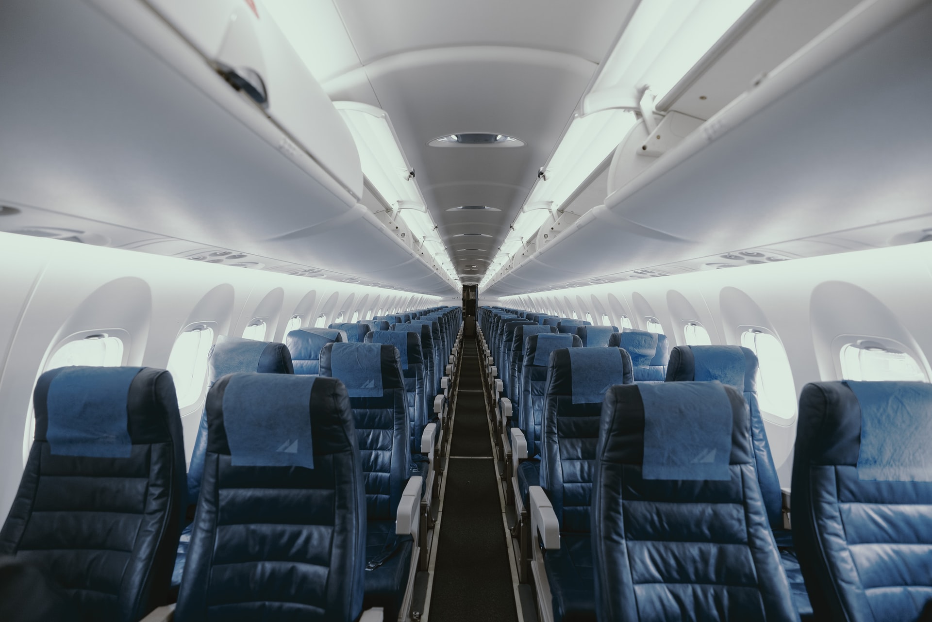 Looking down the rows of an empty airline cabin, with blue seats and white overhead bins