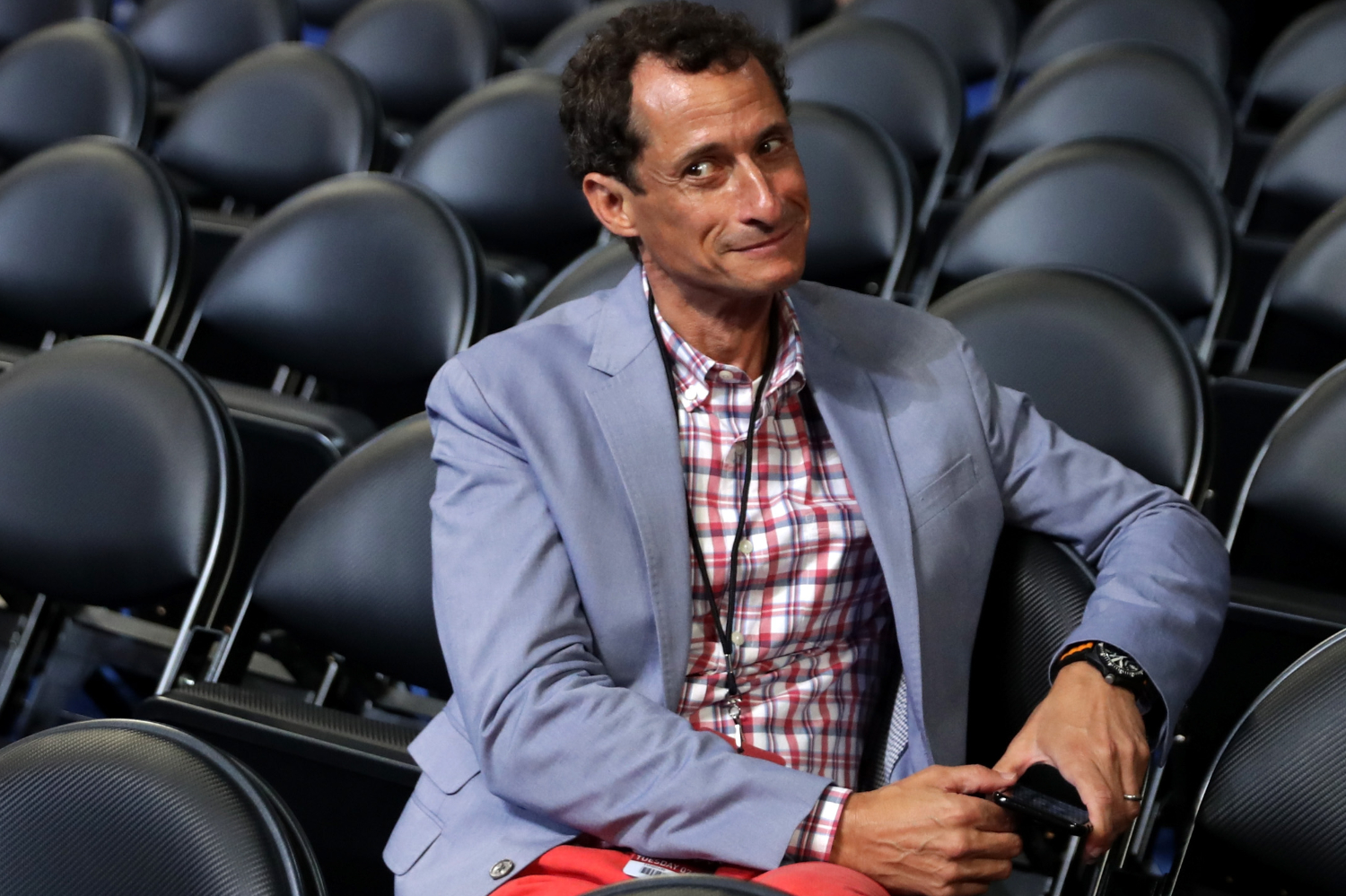 anthony weiner sitting in rows of black folding chairs holding phone