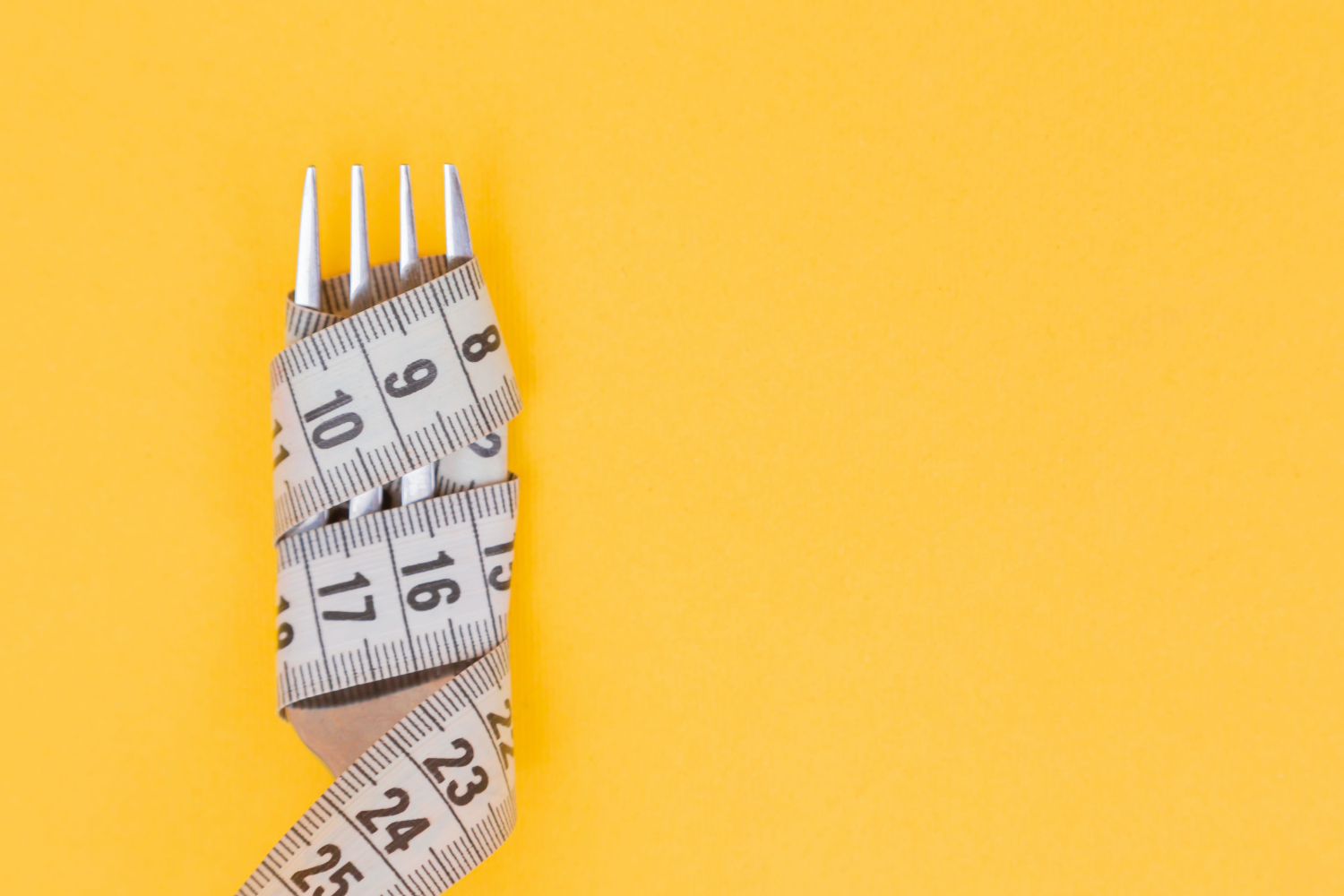 Fork wrapped in tape measure on yellow background