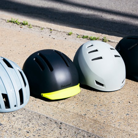 Four stylish, modern bicycle helmets — by Sweet Protection, Thousand, Smith and Bern, respectively — situated in a row on the sidewalk