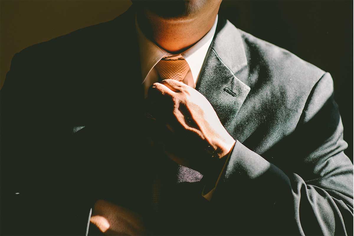 A man in the shadows loosening his tie. A tight tie has been linked to a myriad of health issues.