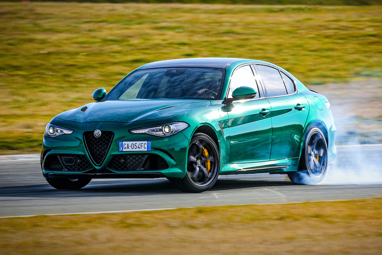 A green 2021 Alfa Romeo Giulia Quadrifoglio sport sedan smoking its tires on a racetrack surrounded by grass