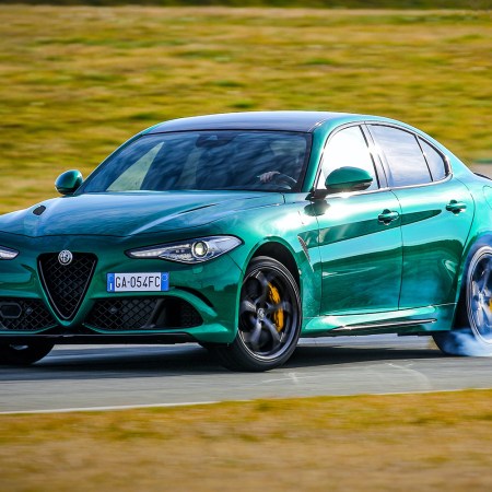 A green 2021 Alfa Romeo Giulia Quadrifoglio sport sedan smoking its tires on a racetrack surrounded by grass