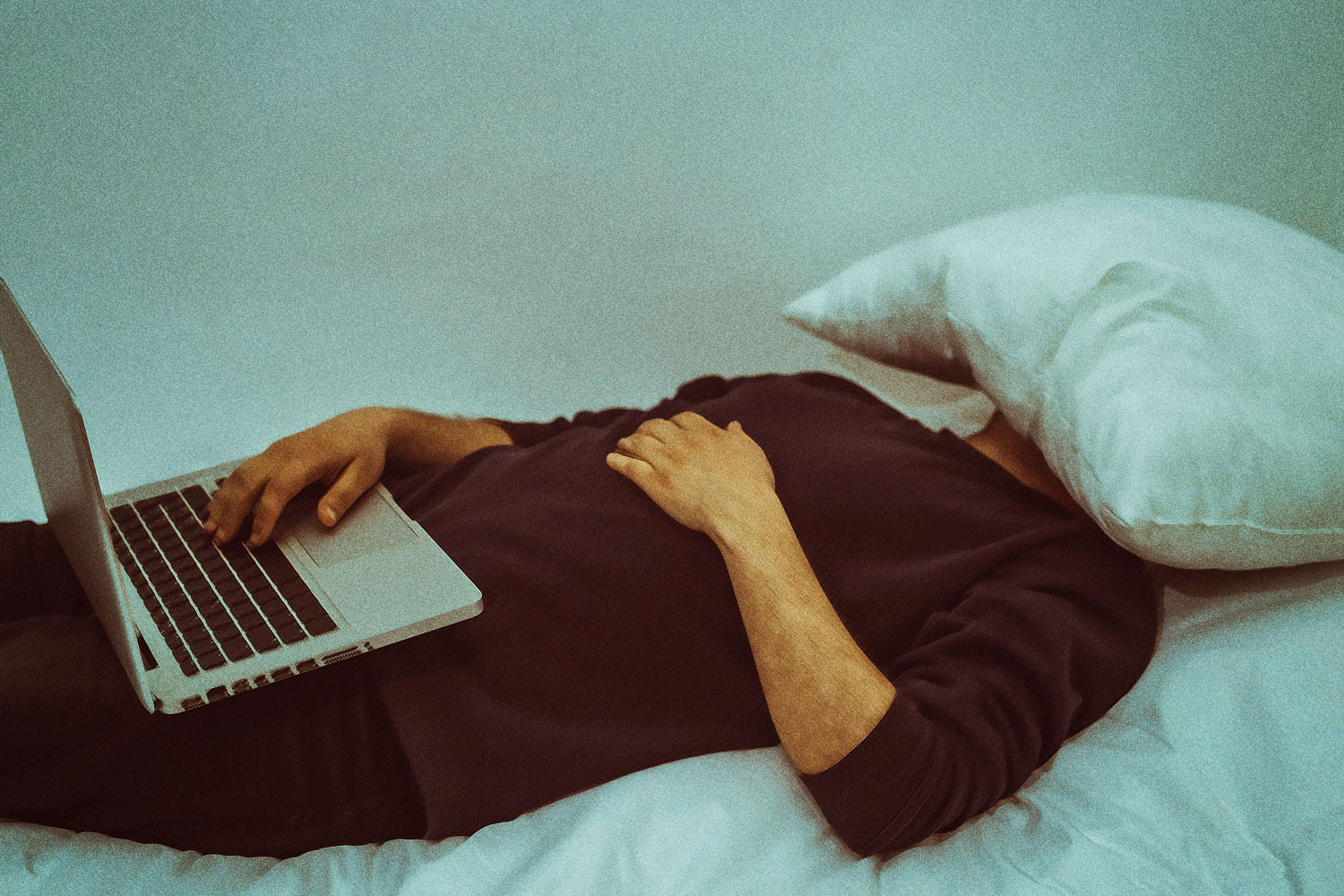 A man sleeps with a pillow on his face and a computer on his lap.