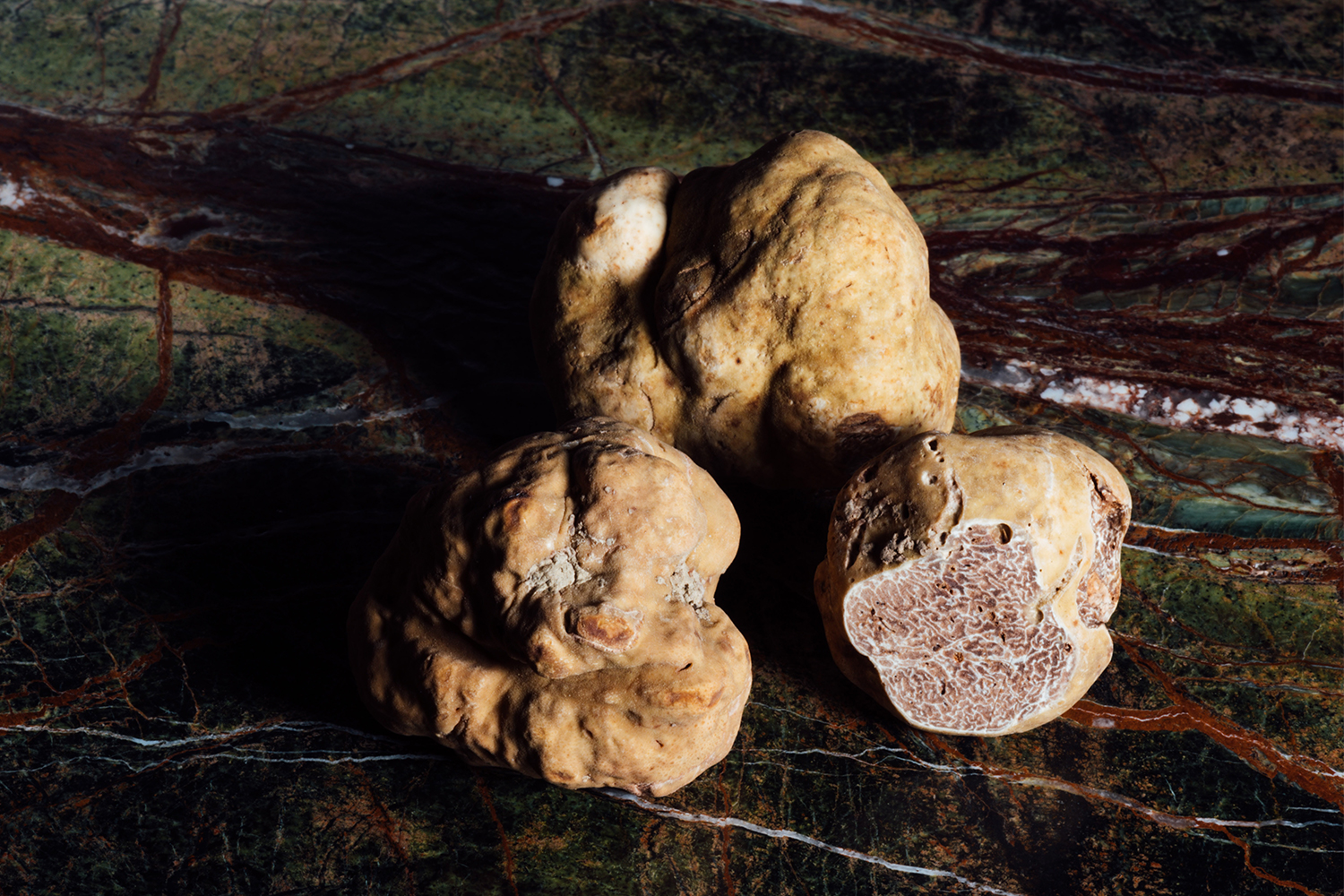 Three white truffles sitting on a table, one of them cut to show the interior of the fungal delicacy