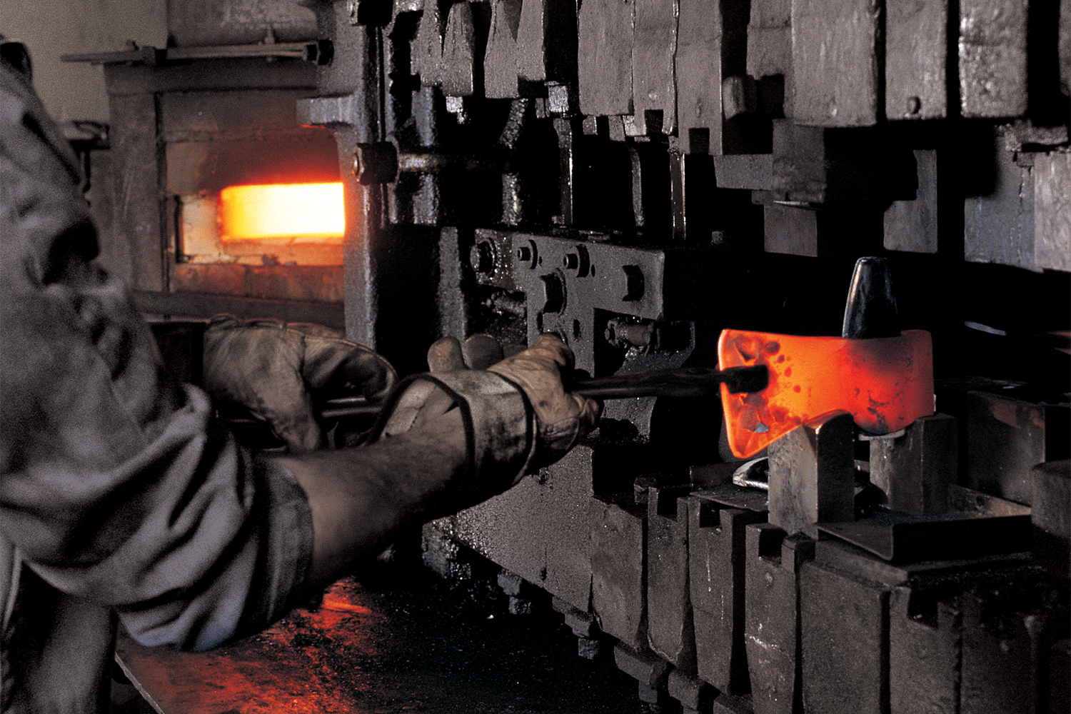 A Hults Bruk forger holding a red hot steel axe head between tongs, forging the tool in the Swedish factory