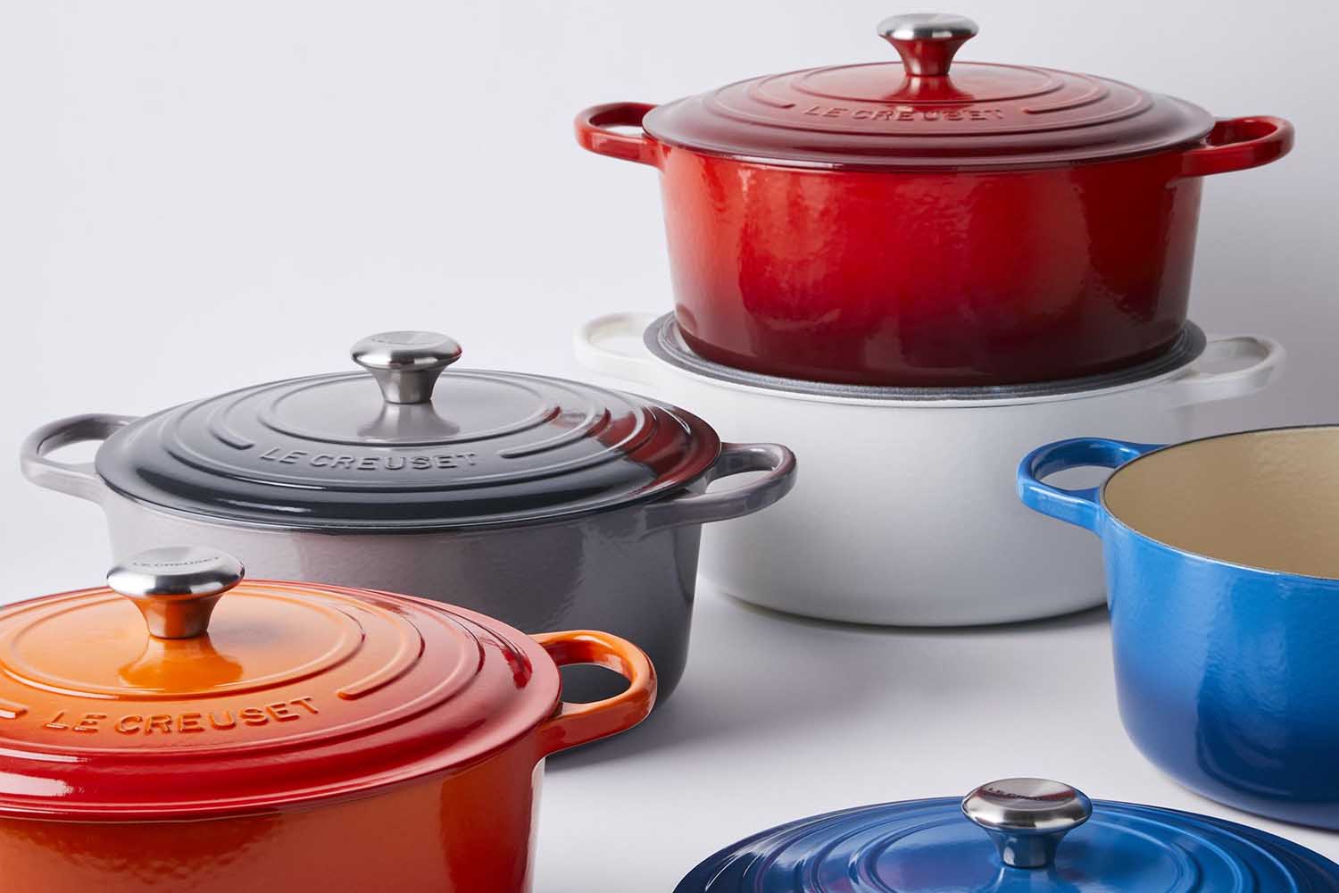 An array of 8-quart Dutch ovens from Le Creuset in red, orange, grey, white and blue on a table