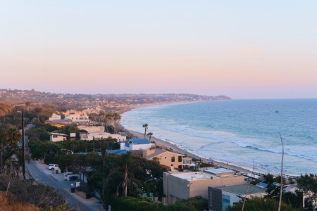 A photo of Malibu, California from above, showing beachfront houses along the ocean