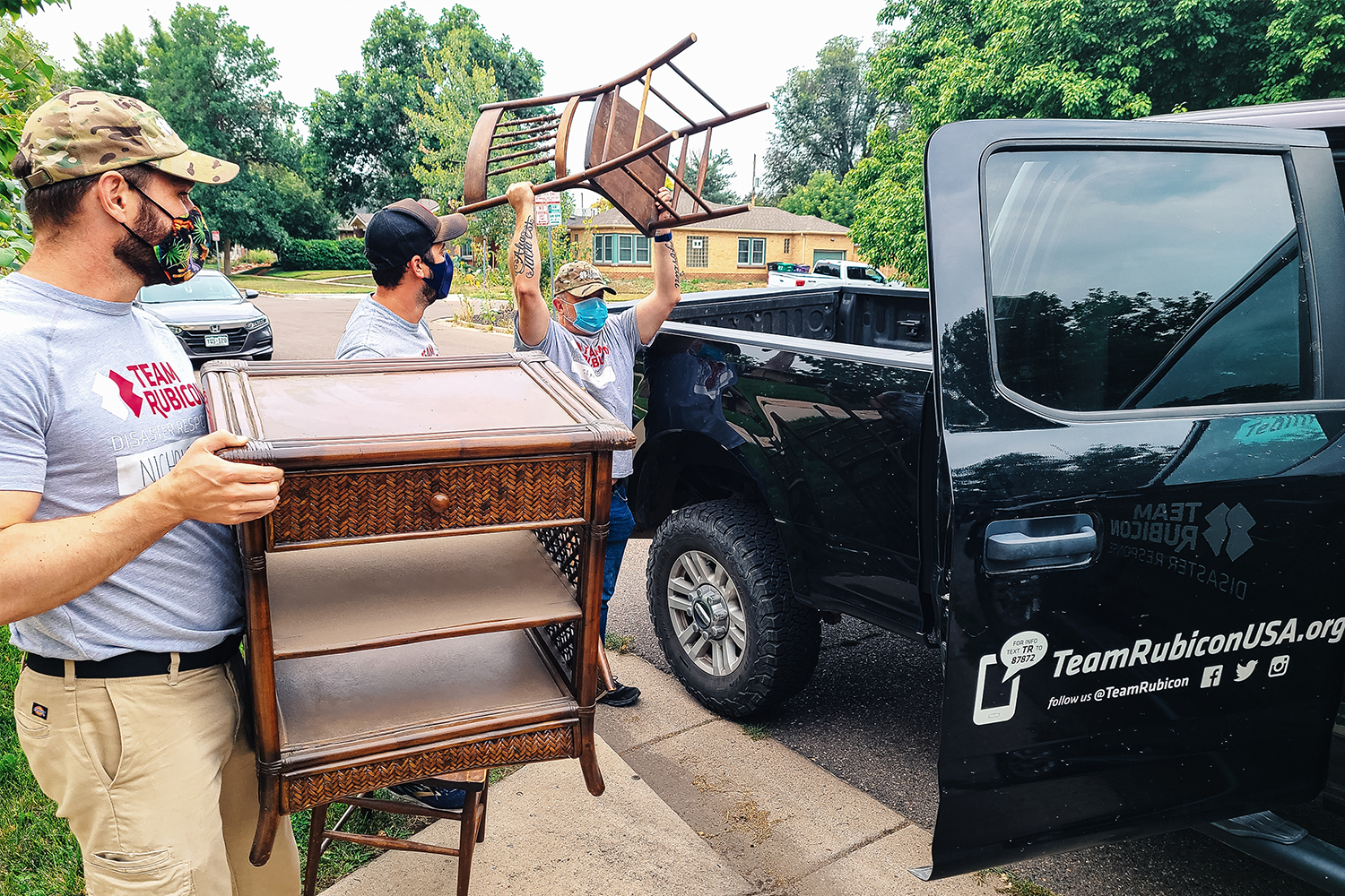 Three Team Rubicon volunteers unloading furniture from a black pickup truck to furnish a home for Afghans resettling here in the U.S.