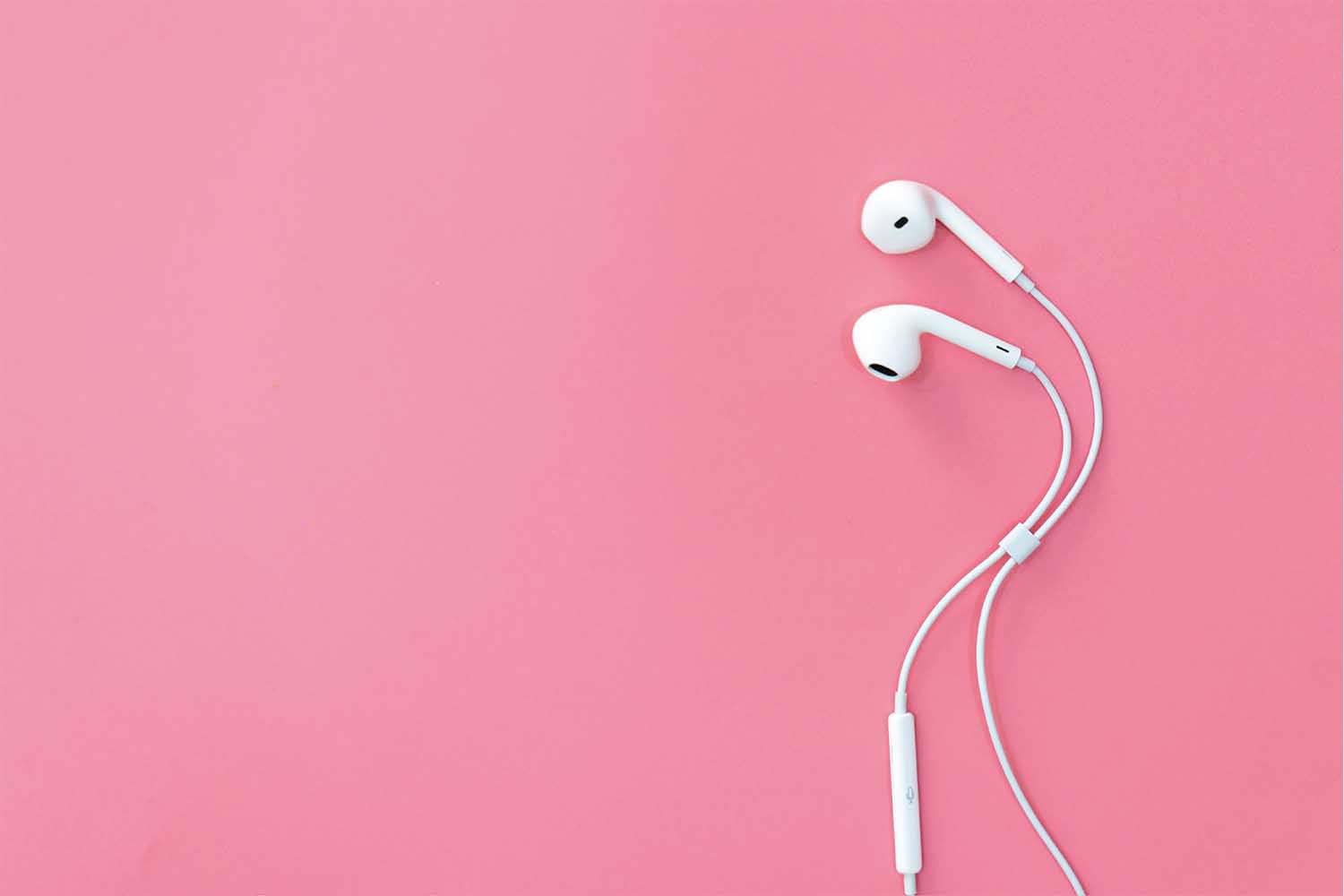 Apple wired headphones on a pink background.