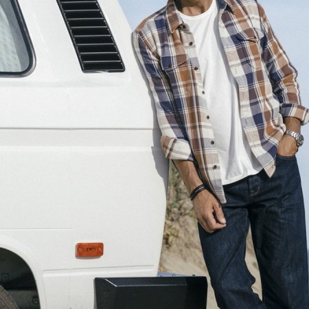 a man in a Outerknown shirt leaning on a car