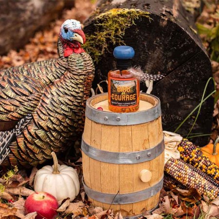 A turkey in a forest near a bottle of Bird of Courage whiskey, a Thanksgiving-themed new spirit from Tamworth Distillery in New Hampshire