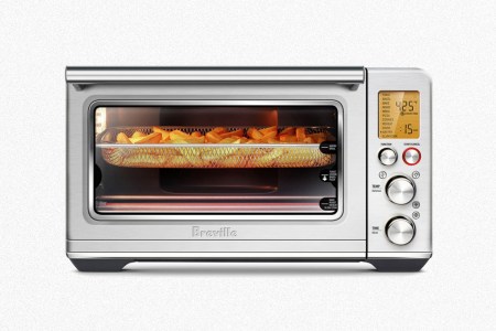 The Breville Smart Oven Air Fryer, with a basket of French fries toasting in the kitchen appliance, on a grey background