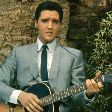 Rock and roll singer Elvis Presley strums his acoutic guitar by a palm tree in circa 1965.