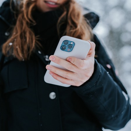 A woman holding an iPhone while standing outside in the snow while wearing a winter coat