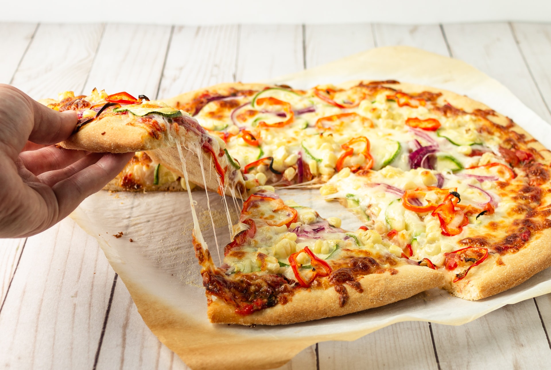 A pizza on a serving platter on a table with a hand reaching down and pulling a slice away